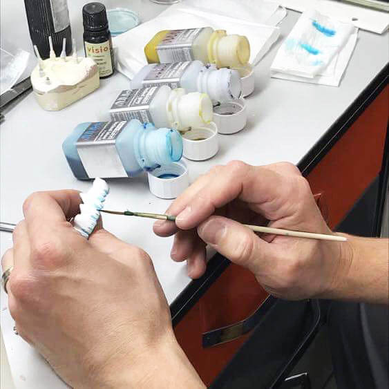 Technician hand-staining a restoration with shade tints
